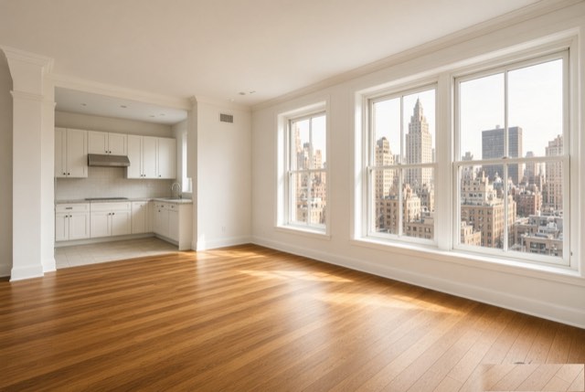 Empty sunlit Manhattan rental apartment with wood floors, white kitchen and city views